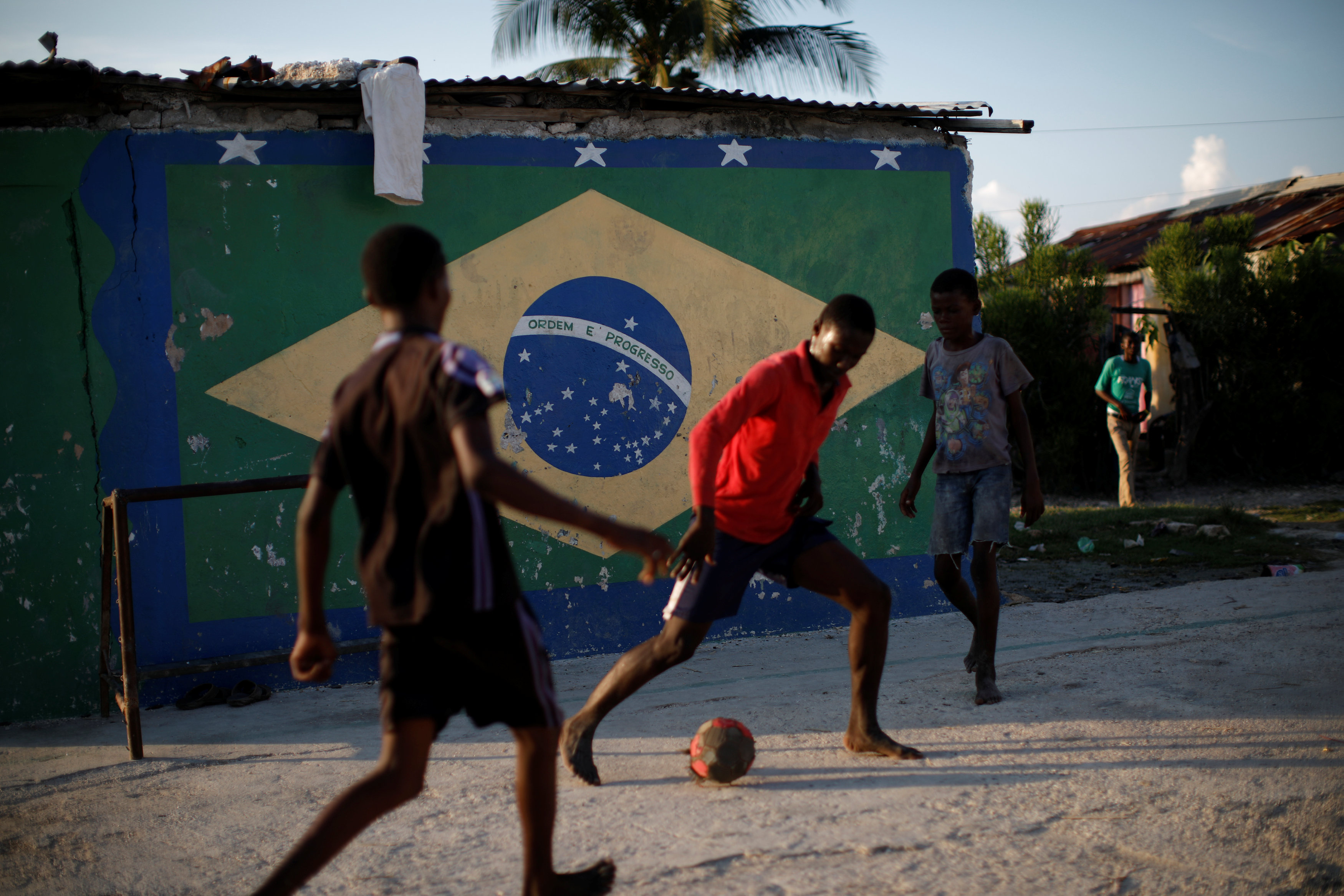 عدد من الفتيان يلعبون كرة قدم فى الحى الذى هاجمه هيلينو ويظهر بالخلفية علم البرازيل