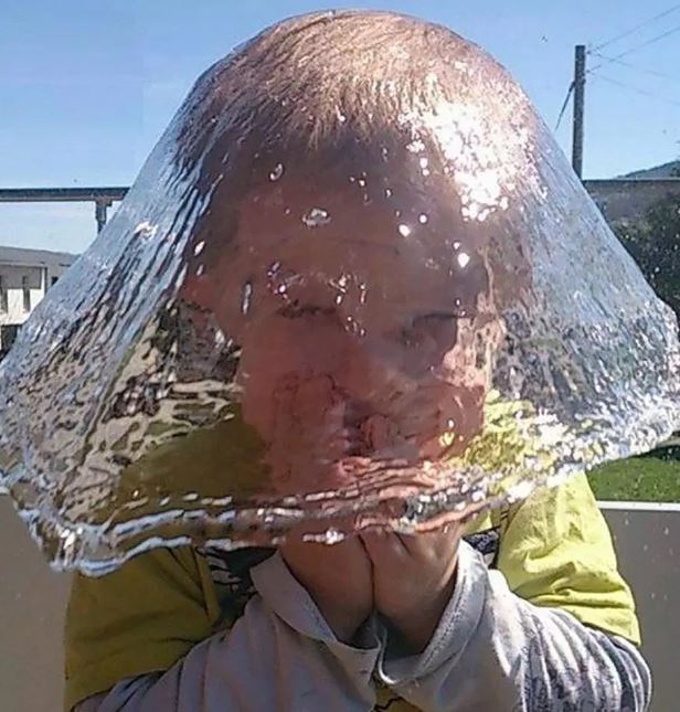 ماء يسقط على وجهه طفل يبدو كأنه مظله