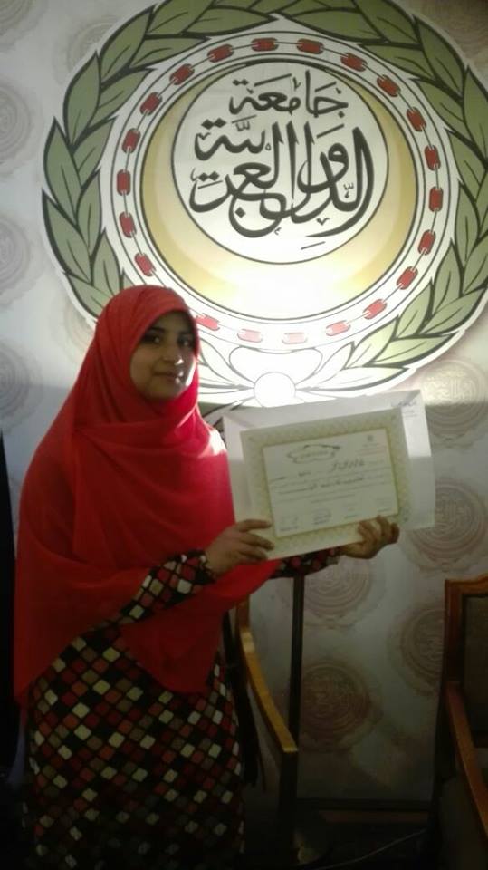 الطالبة مع شعار جامعة الدول العربية بعد فوزها بالمسابقة