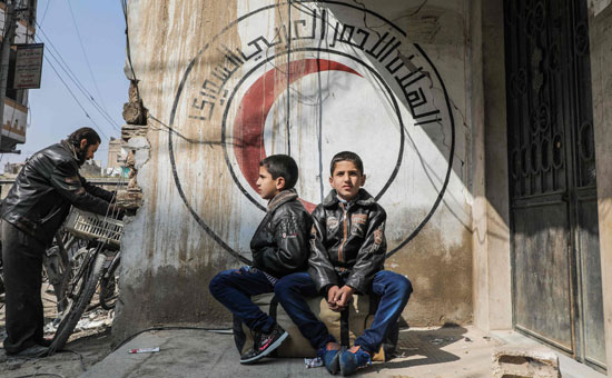 طفلان سوريان يجلسان أمام شعار الهلال الأحمر