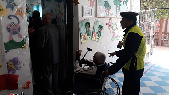 مسن قعيد يساعده احد رجال الشرطة للادلاء بصوته