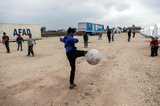 أطفال سوريون يلعبون كرة القدم داخل مخيم للاجئين