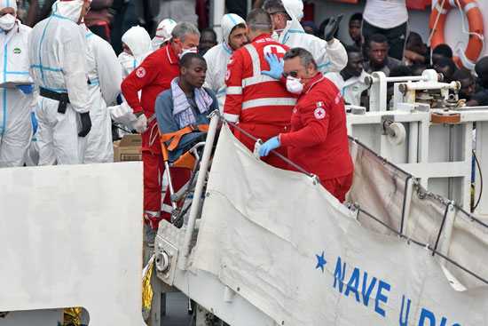 مسعفون يساعدون رجلا على كرسي متحرك قبالة سفينة خفر السواحل الإيطالية عقب عملية إنقاذ للمهاجرين واللاجئين في البحر