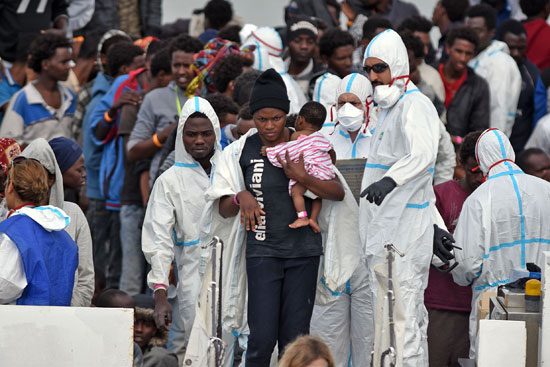 امرأة تحمل طفلاً وهي تنزل من سفينة "خفر السواحل الإيطالية