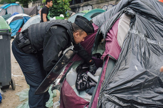 شرطى فرنسى يخلى خيمة للمهاجرين فى باريس