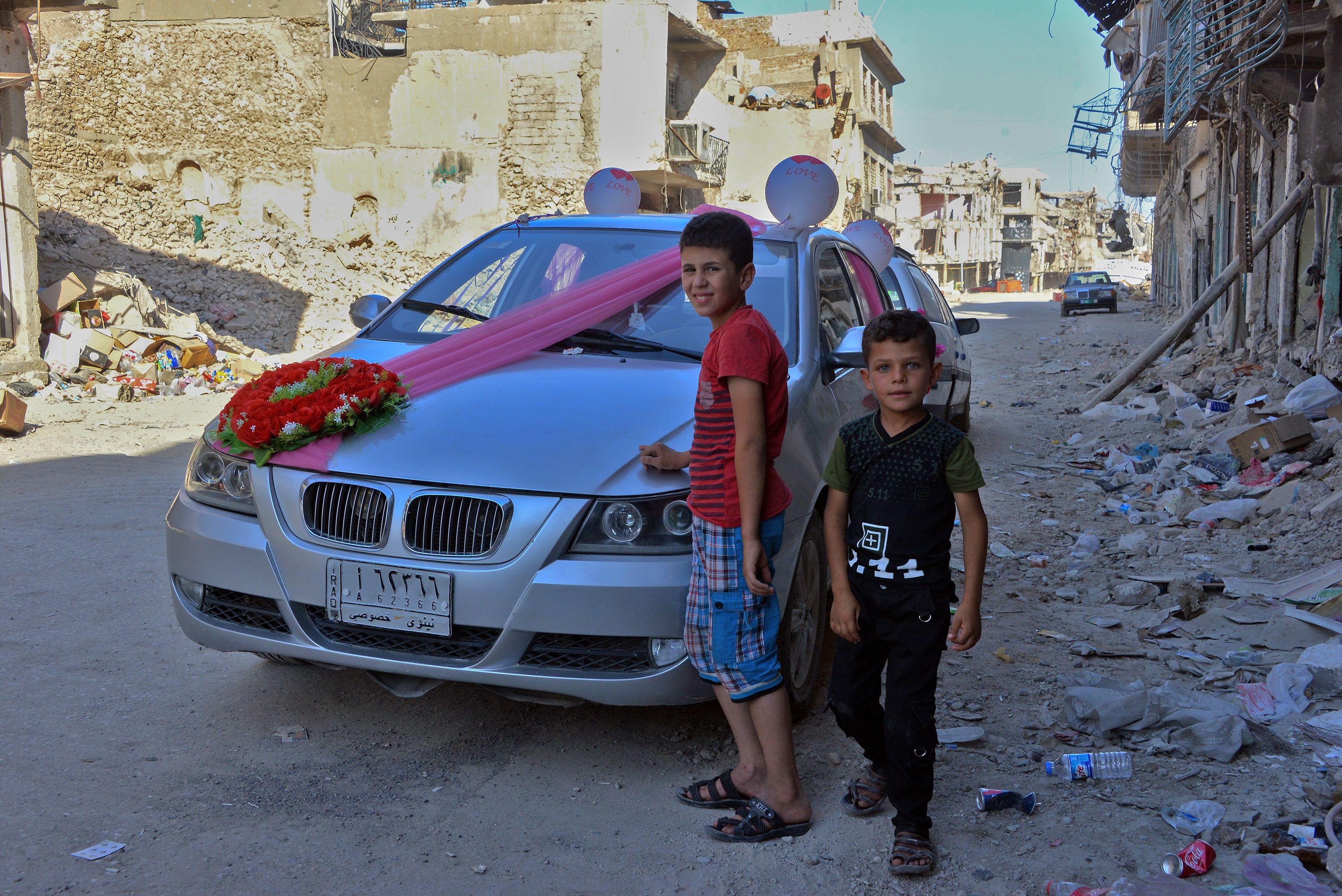 أطفال بجوار سيارة الزفاف بينما يظهر بالخلفية أثار الدمار الذى تركته داعش