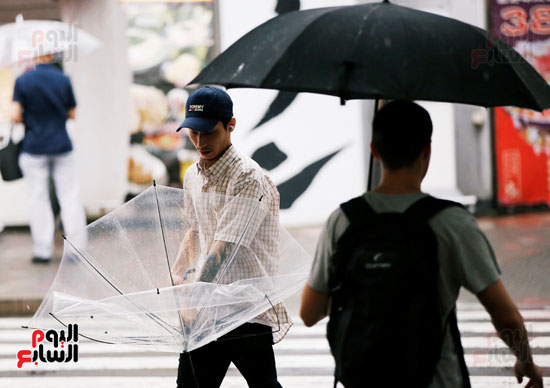 اليابانيون يحتمون من الرياح والأمطار بالمظلات