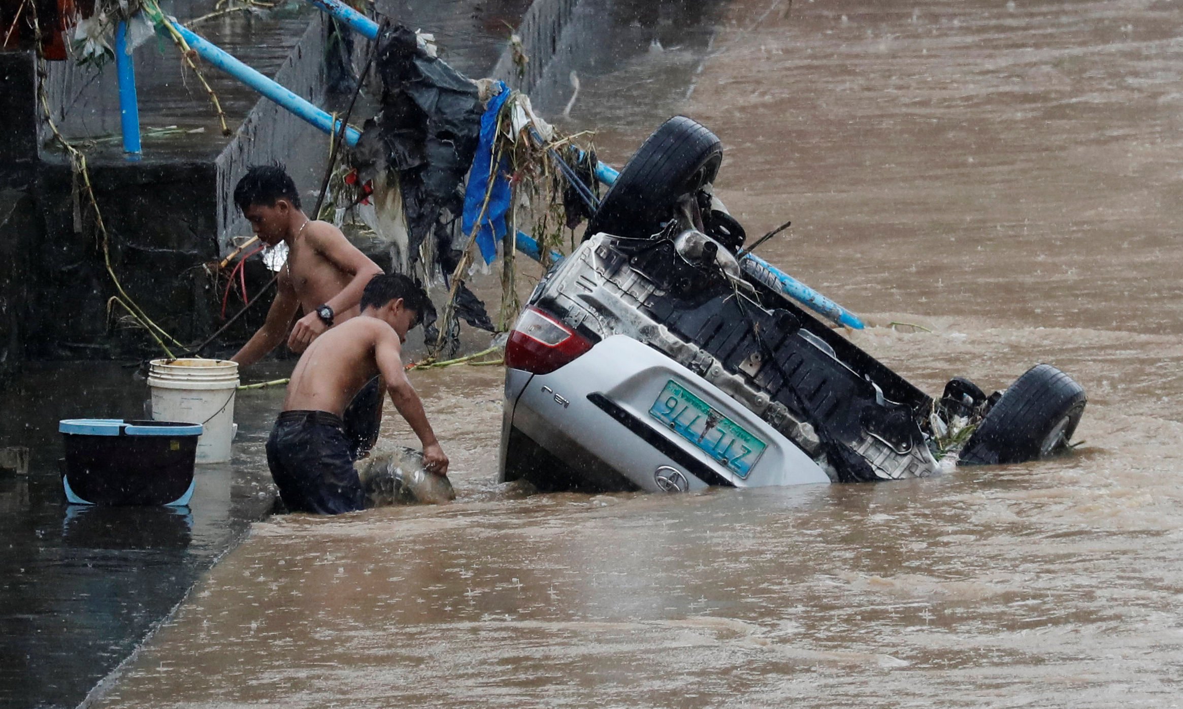 شخصان قرب سيارة انقلبت بسبب الفيضانات