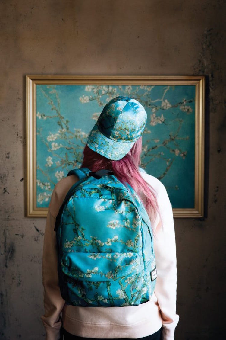 شابة ترتدى طاقية و حقيبة ظهر و تقف أمام لوحة لفان جوخ بنفس اللوحة
