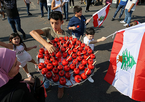 أطفال يحملون العلم الوطنى اللبنانى أثناء قيام صبي ببيع تفاح الكراميل