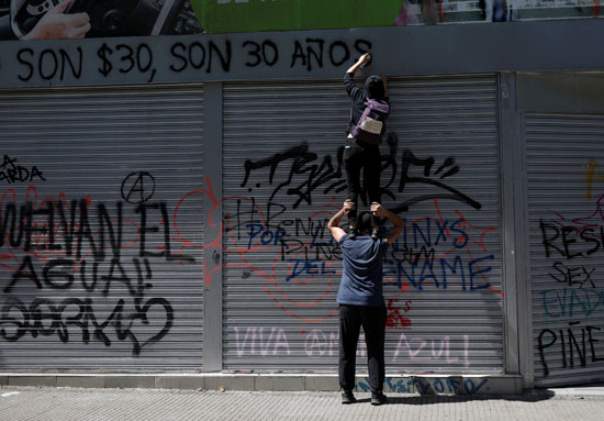 متظاهرون يكتبون عبارات مناهضة للحكومة على الجدران بالشوارع