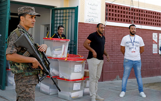 جندي يقف حذرًا أثناء قيام وكلاء الاقتراع بنقل صناديق الاقتراع