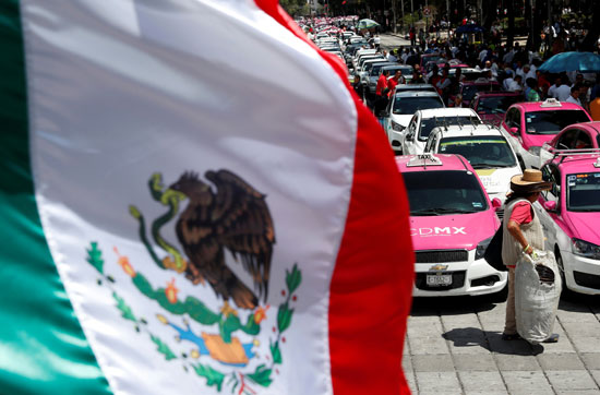 العلم المكسيكي يرفرف بينما ينظم سائقي سيارات الأجرة احتجاجًا على تطبيقات التاكسي الذكية