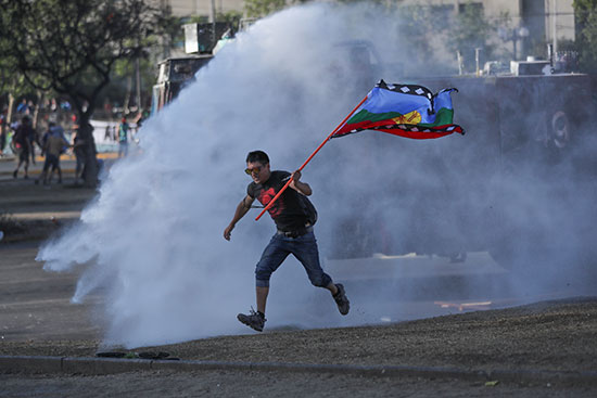 متظاهر يركد ويرفع علم التشيلى بينما تنفجر اسطوانة غاز مسيلة للدموع