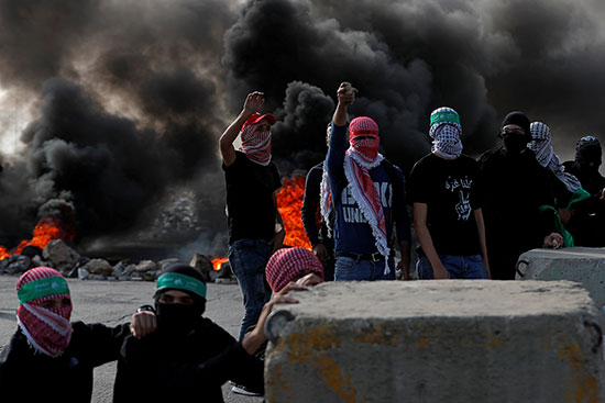 متظاهرون فلسطينيون ملثمون يبدون إشارة خلال مظاهرة مناهضة لإسرائيل