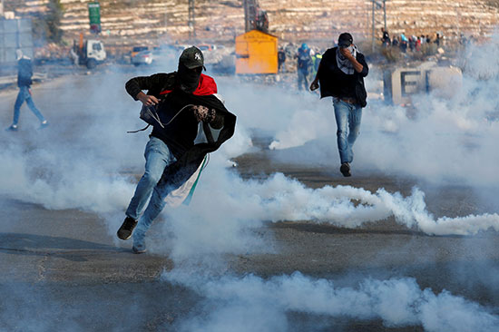 متظاهرون فلسطينيون يفرون من الغاز المسيل للدموع الذي أطلقته القوات الإسرائيلية