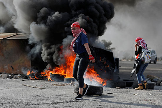 متظاهرة فلسطينية أمام إطارات محترقة أثناء مظاهرة مناهضة لإسرائيل