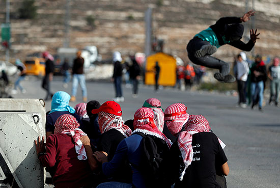 المتظاهرون الفلسطينيون يتسترون بينما يقفز زملائهم خلال مظاهرة مناهضة لإسرائيل