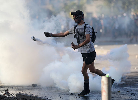 متظاهر يلقى قنبلة غاز مسيل للدموع على الشرطة