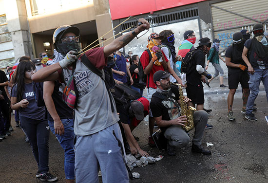 مجموعة متظاهرين واحدهم يقصف الحجارة على قوات الامن