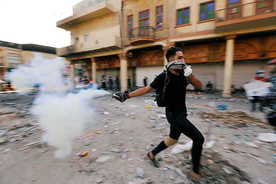 متظاهر عراقي يرمي عبوة غاز مسيل للدموع خلال الاحتجاجات