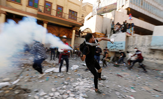 متظاهر عراقي يرمي عبوة غاز مسيل للدموع باتجاه قوات الامن