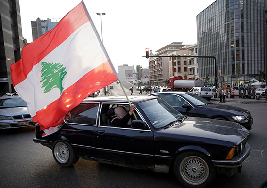 امرأة تحمل العلم اللبناني من نافذة السيارة أثناء قيادتها في وسط بيروت