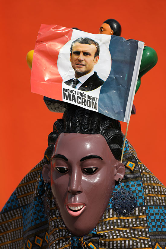 علم صغير يصور الرئيس الفرنسي إيمانويل ماكرون مرفق بقناع قبل وصوله ساحل العاج