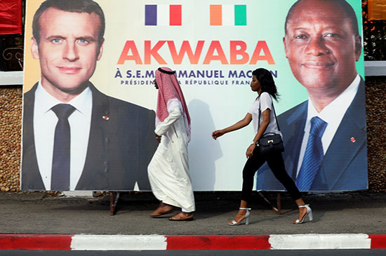 المارة عبر لافتة للرئيس الفرنسي إيمانويل ماكرون ونظيره في ساحل العاج الحسن واتارا