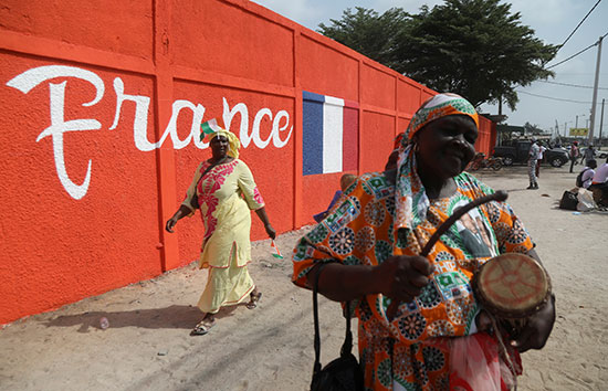نساء يمشون وراء حائط ملون قبل وصول الرئيس الفرنسي إلى ساحل العاج