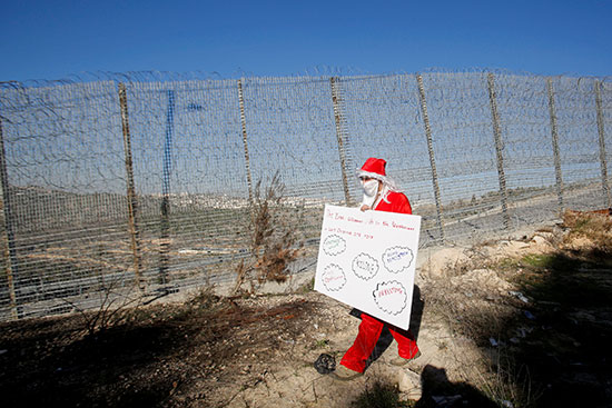 متظاهر فلسطينى يرتدى زى بابا نويل بالقرب من الجدار الإسرائيلى فى الضفة الغربية