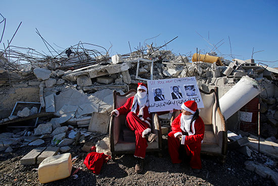 متظاهرون يرتدون زى سانتا كلوز يجلسون أمام بقايا منزل فلسطينى هدم خلال مظاهرة مناهضة لإسرائيل
