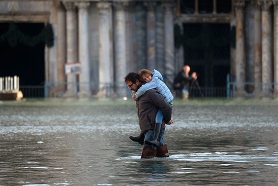 رجلا يحمل ابنه خلال سيره فى مياه الفيضانات