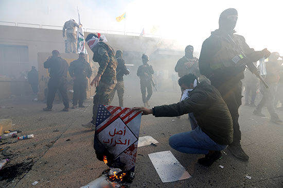 أحد أفراد الحشد الشعبي يحرق ملصقًا أثناء احتجاج لإدانة الغارات الجوية الأمريكية