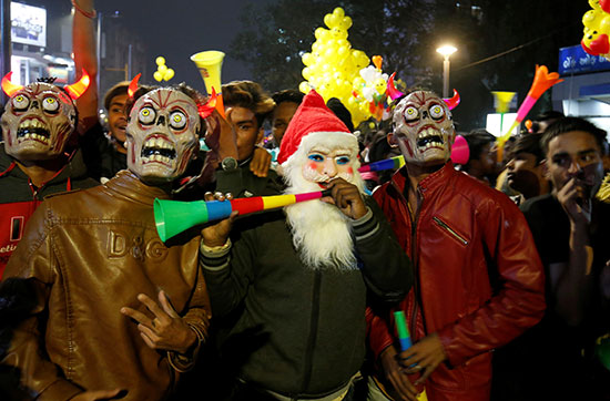 أشخاص يرتدون أقنعة يهبون قرون أثناء الاحتفالات بالترحيب بالعام الجديد في الهند