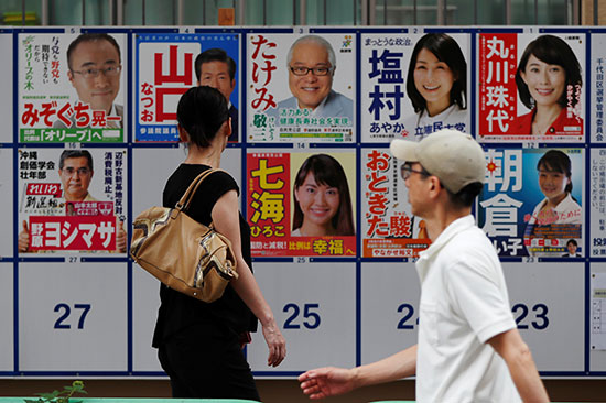 يمشي الناخبون عبر ملصقات الحملة الانتخابية خارج محطة الاقتراع أثناء انتخابات مجلس الشيوخ الياباني في طوكيو
