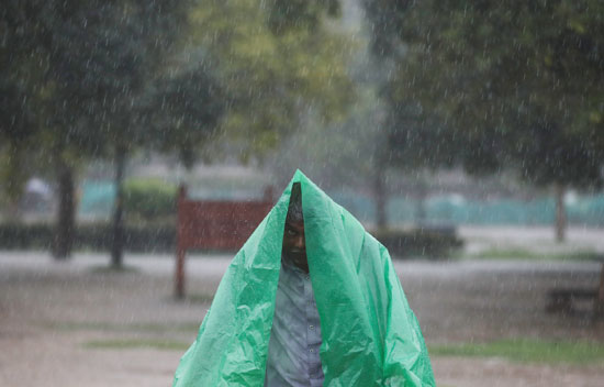 رجل-يستخدم-ورقة-بلاستيكية-لتغطية-نفسه-أثناء-هطول-الأمطار