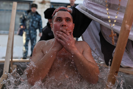 كاهن يقيم حفلاً بينما يغطس نزيل في المياه المتجمدة خلال احتفالات العيد المسيحي الأرثوذكسي ا