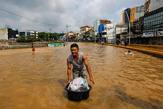 رجل يحمل أمتعته ويسير عبر مياه الفيضان