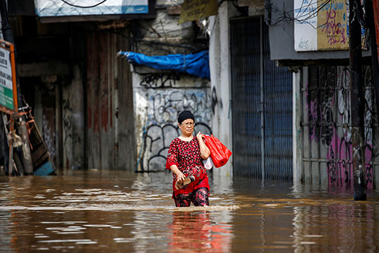 امرأة تحمل متعلقاتها تسير عبر مياه الفيضان