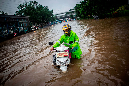 رجل يمشي مع دراجته البخارية عبر مياه الفيضان بعد هطول أمطار غزيرة في جاكرتا