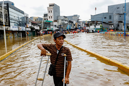 رجل يستخدم العكازات للمشي في مياه الفيضان