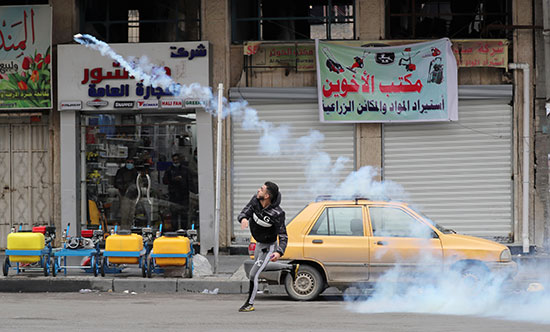 متظاهر يرمي علبة غاز مسيل للدموع على قوات الأمن العراقية