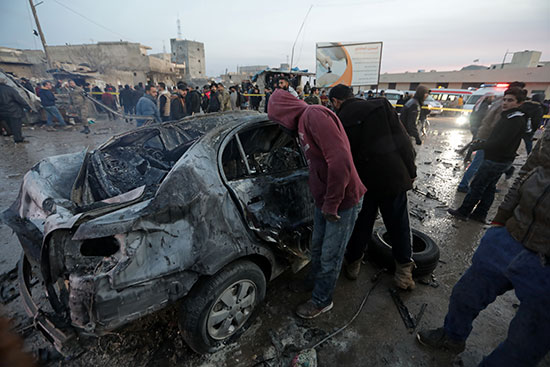 أشخاص يتفقدون سيارة محترقة في موقع انفجار شاحنة في عزاز