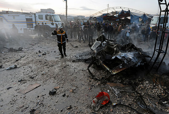 أشخاص يقفون بالقرب من سيارة محترقة في موقع انفجار شاحنة في عزاز