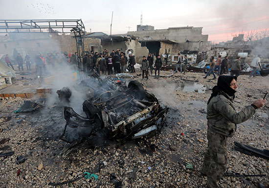 رجل يلتقط صورة بالقرب من سيارة محترقة في موقع انفجار شاحنة في عزاز