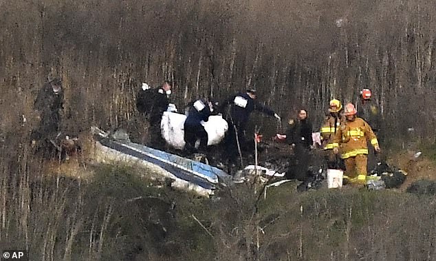 23919068-7933565-Rescuers_retrieve_a_body_from_the_scene_of_the_helicopter_crash_-a-69_1580120364497