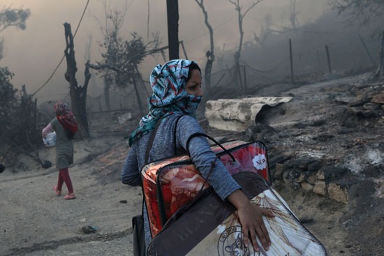 مهاجرة تحمل متعلقاتها بعد اندلاع حريق في مخيم جزيرة ليسبوس