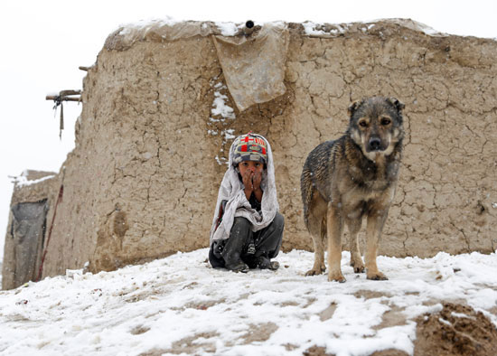 طفل-يجلس-مع-كلبه-بجوار-كوخ-تغطيه-الثلوج