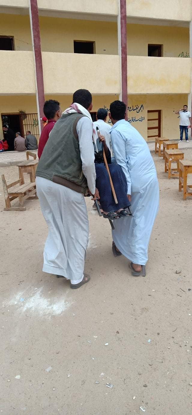 شباب يحملون سيدة مسنة للإدلاء بصوتها